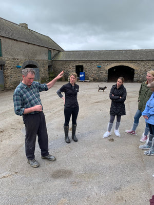 Group with farmer, in an old farmyard. Dog in the background